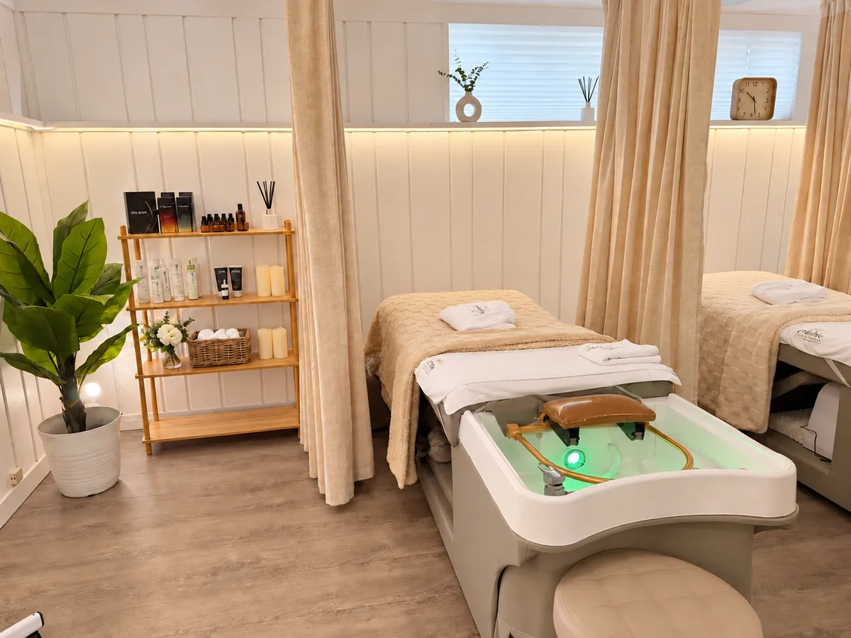 Three cream head spa stations at Aura in Issaquah, with a lit basin, curtain dividers, plants and a shelf of treatment products